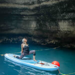 A woman doing stretches on top of a paddle board inside a cave
