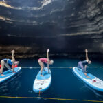 Three people doing yoga on top of paddle boards inside a cave
