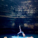 A woman doing yoga on top of a paddle board inside a cave  
