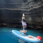 A woman doing a headstand on top of a paddle board inside a cave