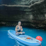 A woman sitting cross-legged on top of a paddle board inside a cave