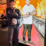 A man standing beside an image of Gordon Ramsay in Hell’s Kitchen