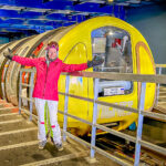 A woman in a pink jacket posing in front of a yellow cable car